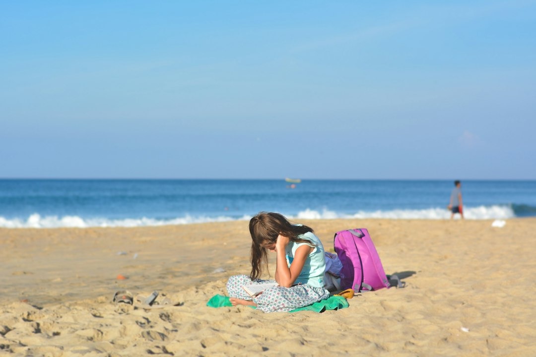 Girl reading a book while sitting on the sandy beach.